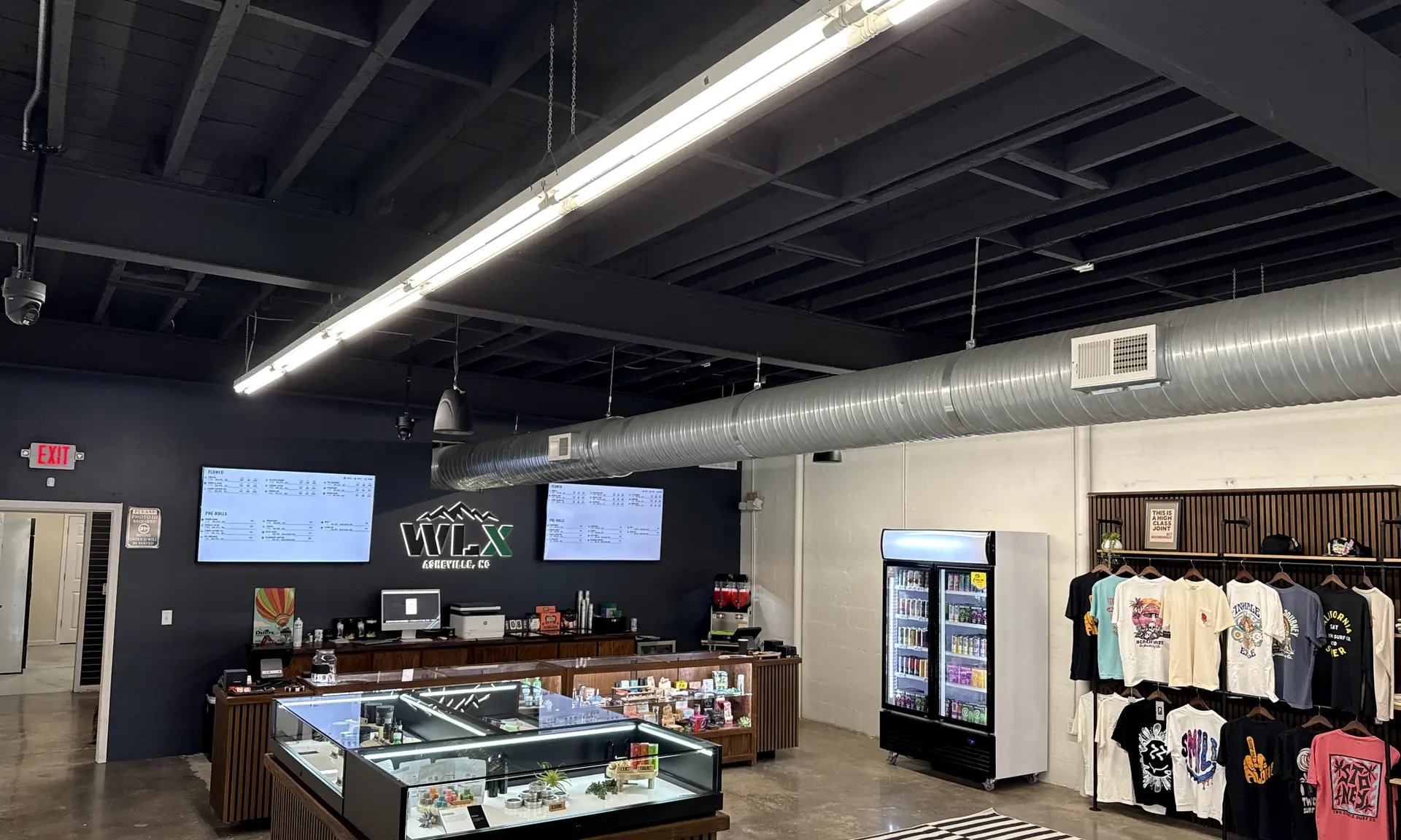 The sales floor at White Label Exotics in Asheville: menu screens and the shop sign on a dark wall, walnut display cases, a drinks cooler and a wall of merchandise.